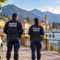 Due guardie giurate sul lungolago con logo Confintesa Sicurezza Privata in trasparenza. Immagine illustrativa generata con IA.